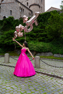 An enchanting Quinceañera strikes a pose during her Quinceañera photoshoot, donning a lovely pink dress while delicately holding her 15th birthday balloons.