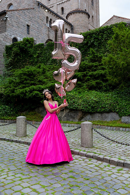 The Quinceañera girl gracefully holds her 15th birthday balloons, adorned in a pink dress and a sparkling tiara.