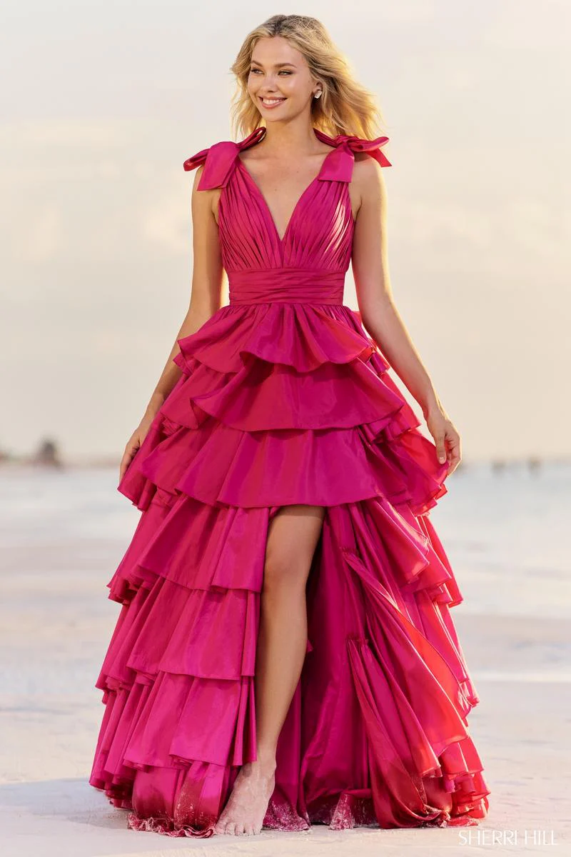 A Sweet 16 girl in a dark pink dress walks barefoot on the beach, her feet in the sand, with the sun shining through her golden hair during a photo shoot in New Jersey.