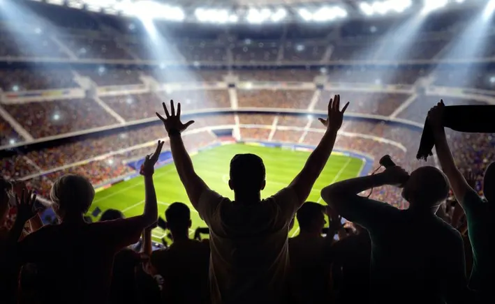 Man with both hands in the air, looking down at a stadium during a football game.