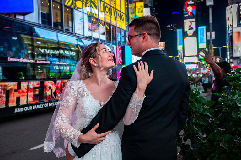 A couple on their wedding day is standing in Times Square holding hands and gazing into each other's eyes.
