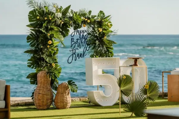 Destination celebration: Celebrating a milestone: an image displaying 'Happy Birthday, Frank' with the number 50, set against an ocean backdrop and green grass in the foreground.