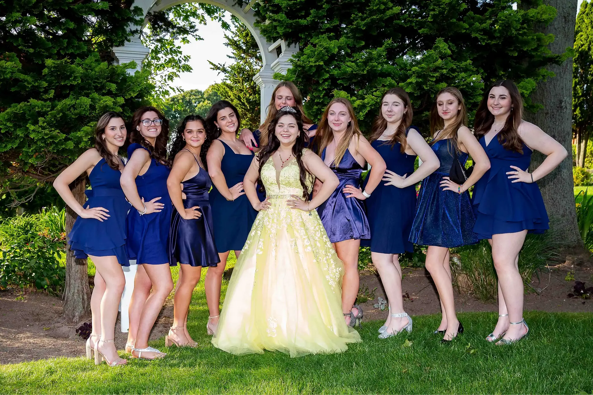 NJ Sweet 16 celebrant wearing a yellow gown posing outdoors with friends in navy blue dresses, all with hands on their waist.