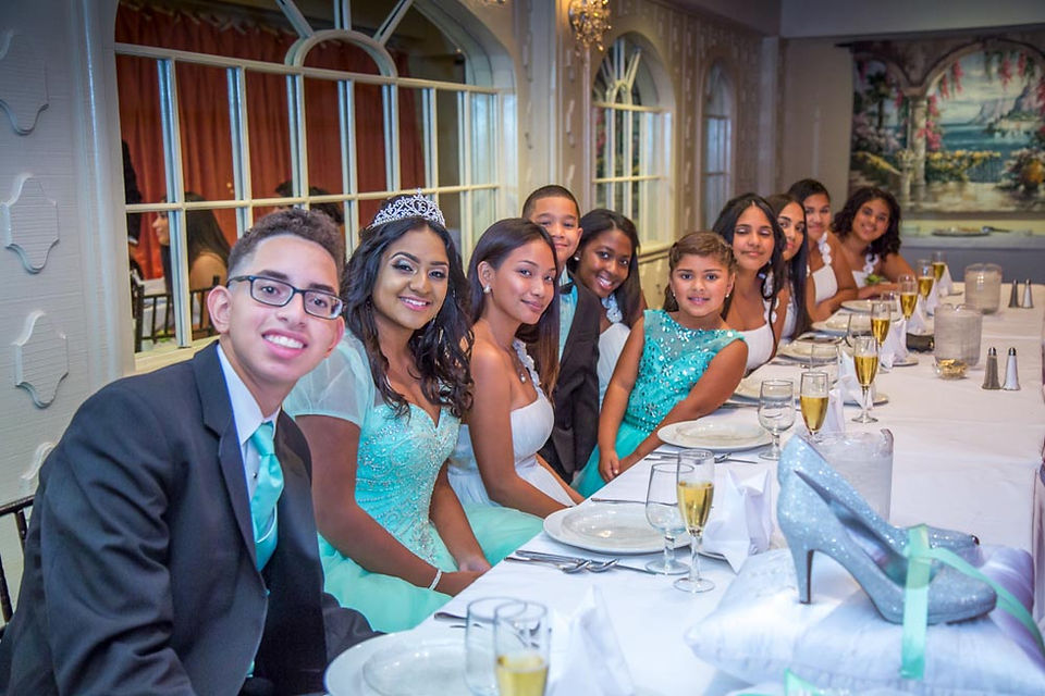 Sweet 16 birthday girl in a green dress and tiara posing at a dinner table with her friends during her New Jersey celebration.