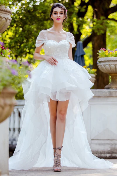 A Sweet 16 girl wearing a white high-low hem dress and red lipstick, posing against a blurred green background before her birthday celebration in NYC.