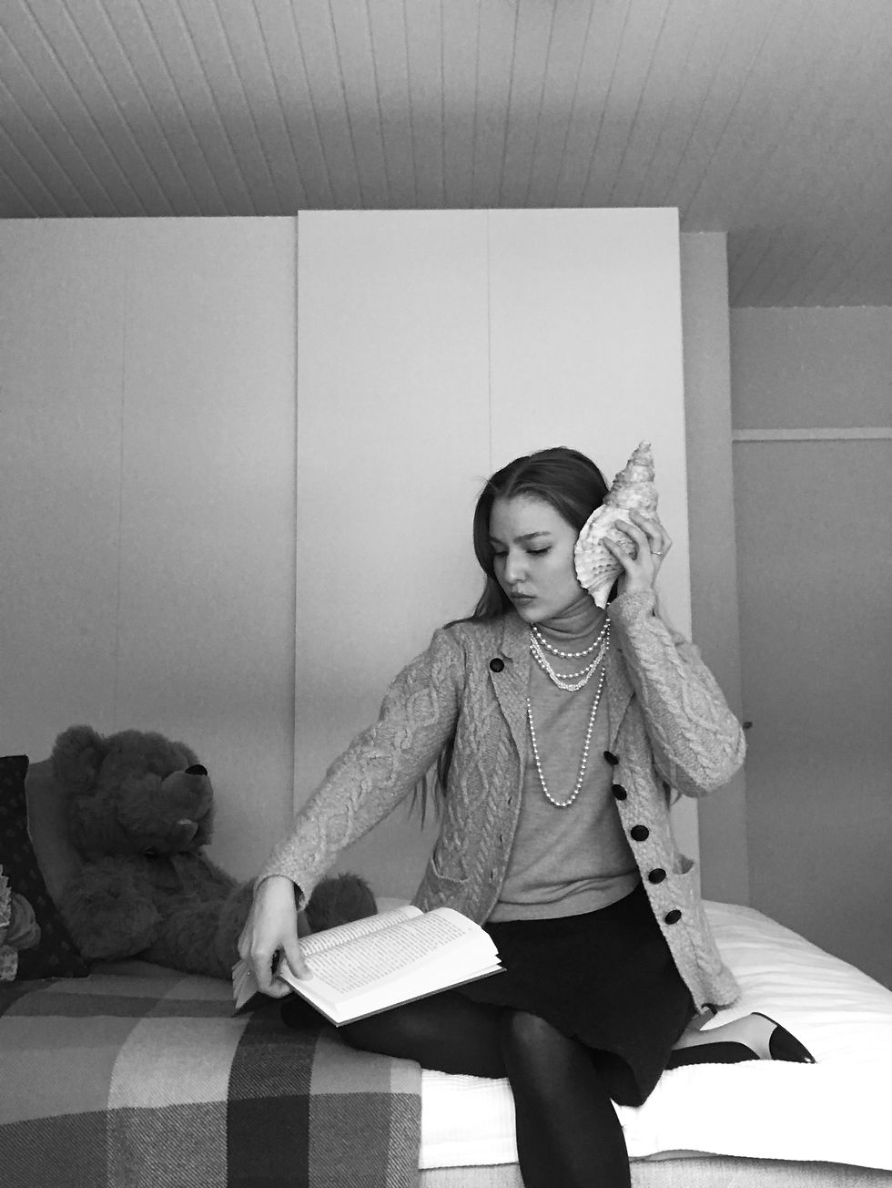 A girl sitting in her bedroom and reading a book.