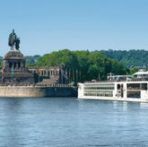 El barco fluvial Viking Bestla navegando por el río Rin frente al monumento ecuestre del Kaiser Guillermo I en Koblenz, Alemania, en un día soleado con cielo despejado.
