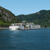 El barco fluvial Viking Freya navegando por el río Rin en la garganta de Loreley, Alemania, con escarpados acantilados de pizarra y colinas boscosas a ambos lados del río en un día soleado.