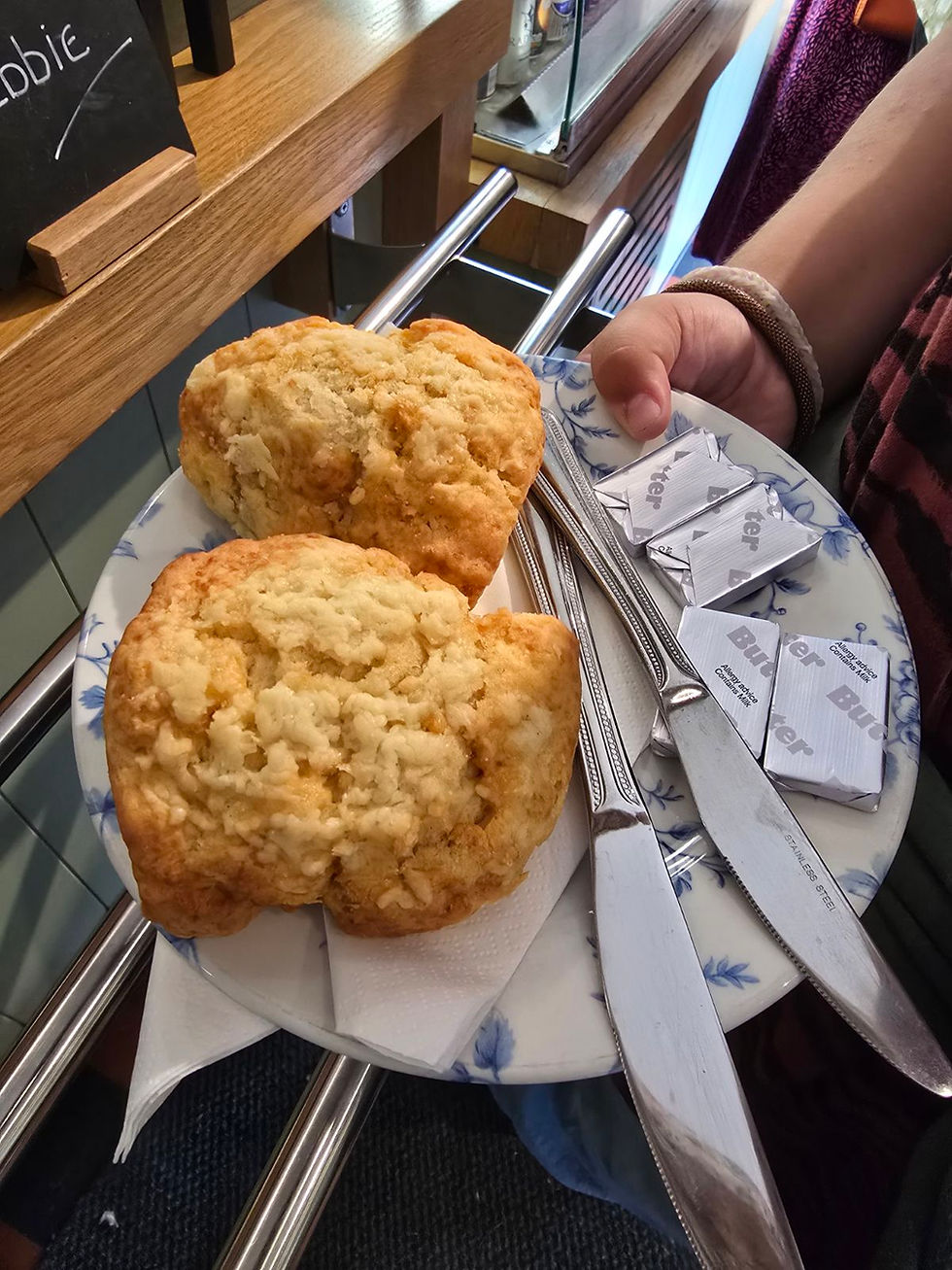 A plate with two cheese scones, two knives and four small packs of butter on it.
