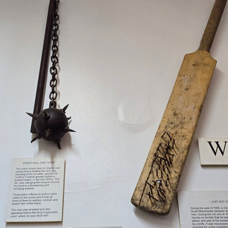 Police museum display of a flail and wooden cricket bat.