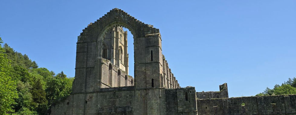 Stone ruins of Fountains Abbey against a clear blue sky.