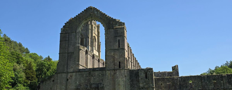 Stone ruins of Fountains Abbey against a clear blue sky.
