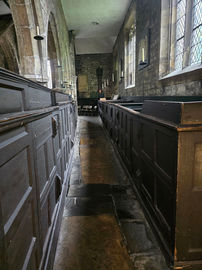 The aisle inside the church looking towards the sunken chapel. Either side of the aisle are dark stained wooden box pews.