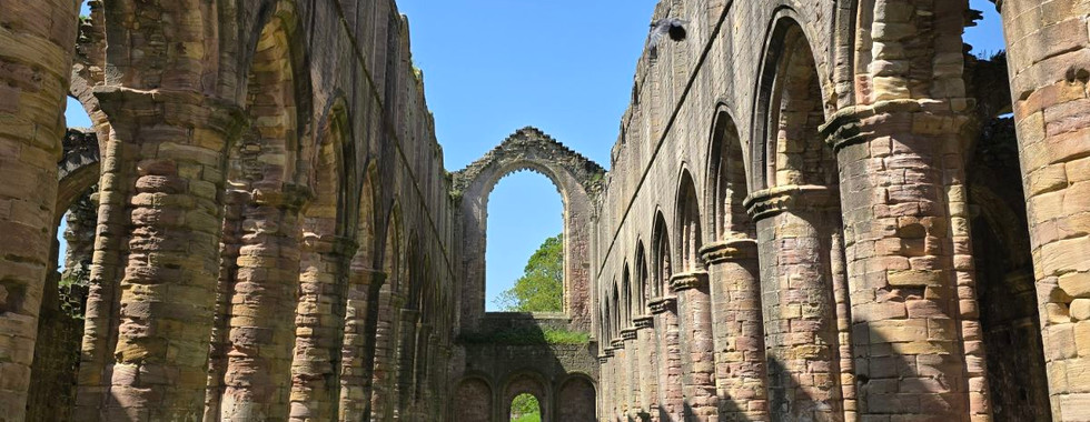The ruins of the nave at Fountains Abbey with stone arches.