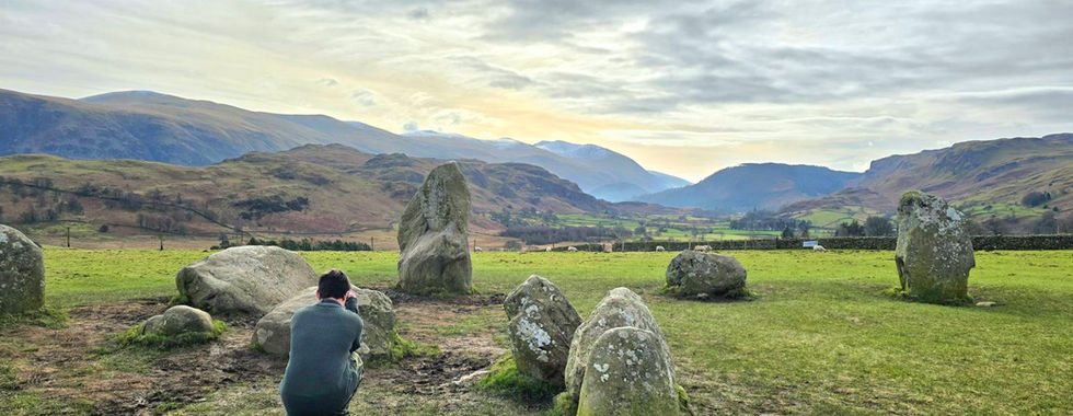 Our son, crouching to take photographs at Castlerigg Stone Circle with mountains in the background.