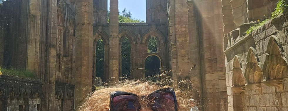 Person at Fountains Abbey stone ruins on a sunny day.