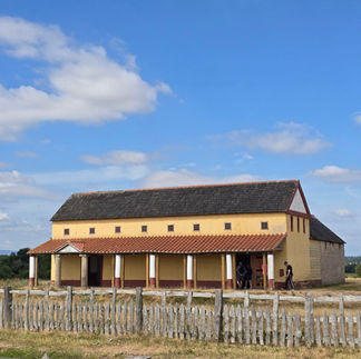 The reconstructed Roman Villa. The sky behind it is blue. The grass in front is yellowed and dry.