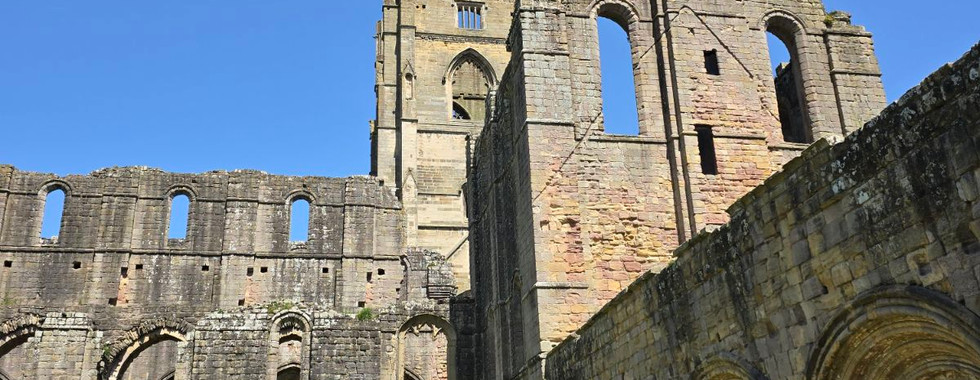 Stone ruins of Fountains Abbey under a clear blue sky.