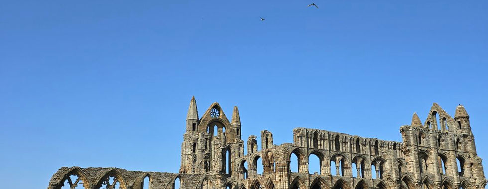Stone ruins of Whitby Abbey under a clear blue sky.