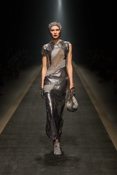 Look futurista com vestido prateado assimétrico e textura metálica que mistura estética armorial com códigos contemporâneos da moda inspirada no medievalismo.