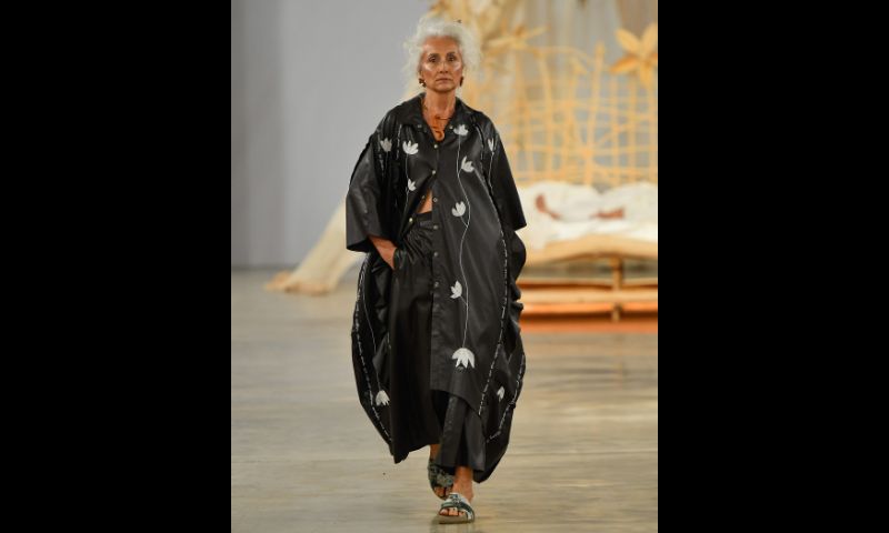 modelo desfila com macacão camisa oversized preta, com estampa floral branca, usando calças pretas.