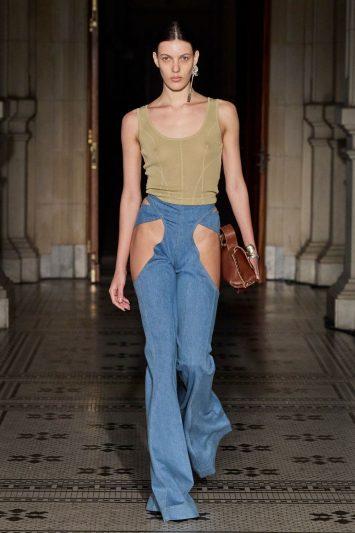 Modelo desfila com regata bege, calças jeans recortadas na altura da pélvis.