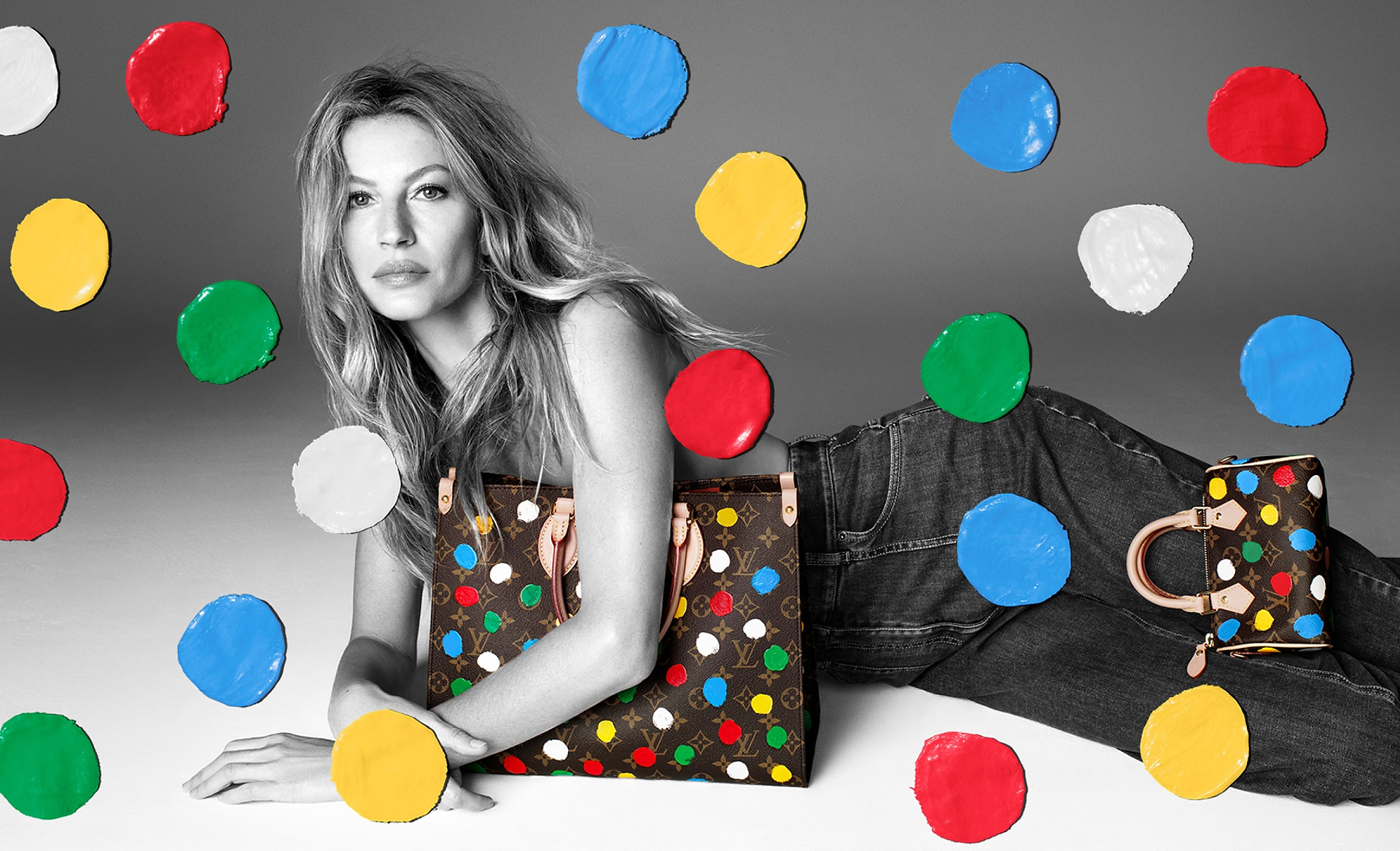 Gisele Bündchen segurando uma bolsa Monogram com polka dots coloridos, usando jeans e posando contra um fundo preto e branco com pontos coloridos flutuantes.
