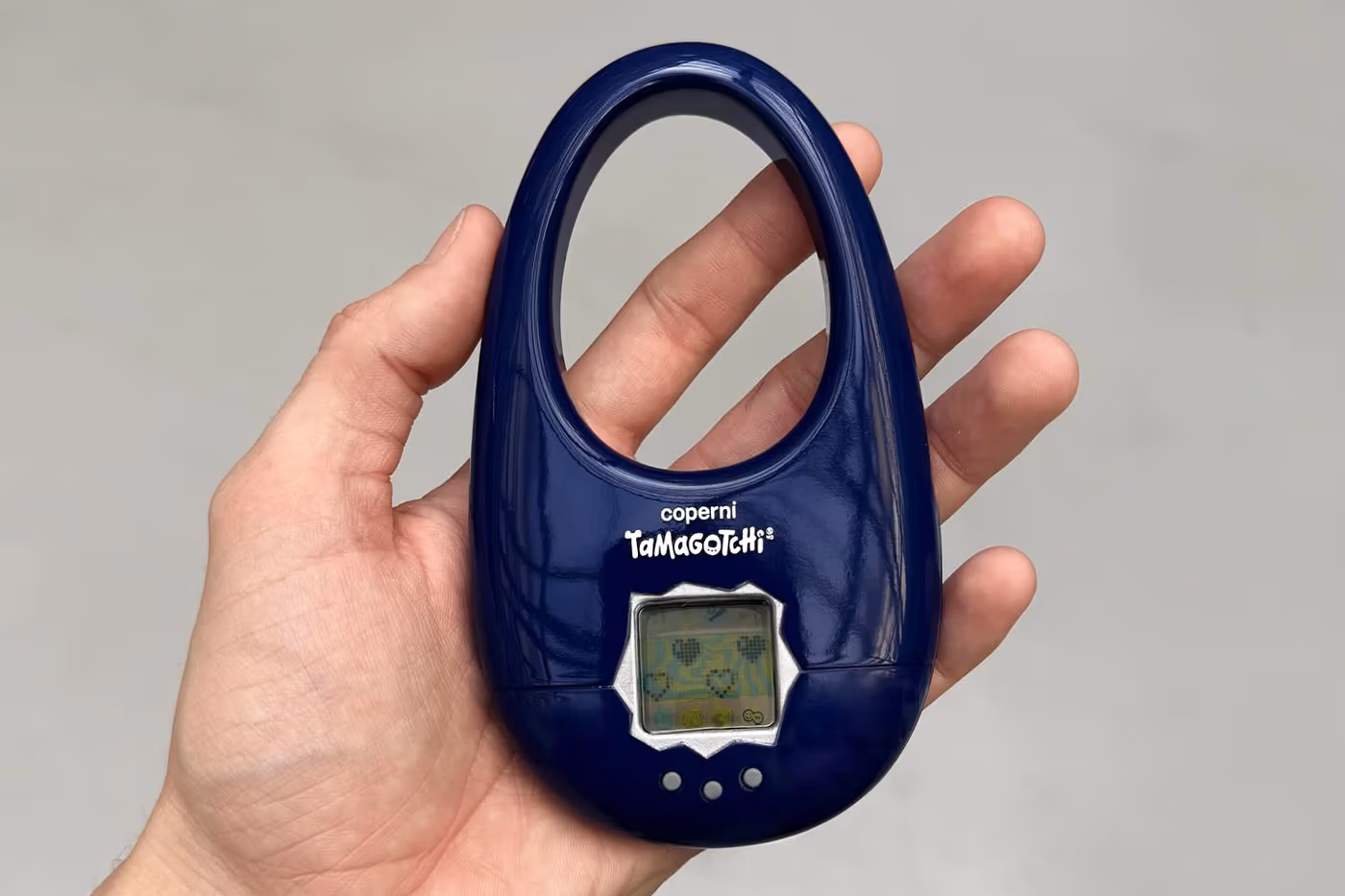 Bolsa Coperni em versão navy com Tamagotchi centralizado, apresentada em close com iluminação direta.