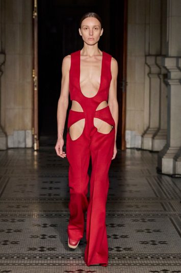 Modelos desfila com macacão vermelho decotado, com recortes no abdome e pélvis.