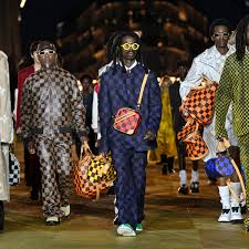 Grupo de modelos na passarela usando looks quadriculados em cores vibrantes, como azul e verde, segurando bolsas combinando, desfilando sob a iluminação noturna de Paris.