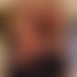 Donata Meirelles sorrindo em um ambiente aconchegante ao lado de um homem de óculos e uma mulher de cabelo castanho. Os três estão abraçados, vestindo roupas em tons neutros.