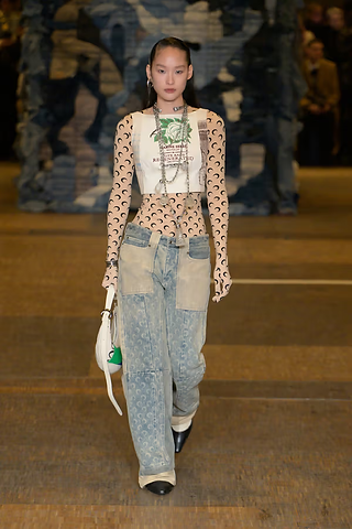  Modelo desfilando com um catsuit de estampa de lua crescente combinado com jeans reaproveitado, transmitindo a fusão entre esportivo e couture na estética de Marine Serre.