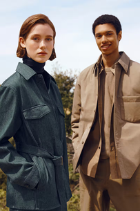 Dois modelos, um vestindo uma jaqueta jeans verde militar e outro usando um conjunto bege de algodão com camisa e calça de alfaiataria.