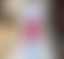 Modelo com look de alfaiataria azul claro sobreposto a peças vermelhas vibrantes, finalizando com óculos futuristas e bolsa marrom.