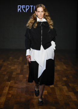 Modelo na passarela usando look preto e branco assimétrico da Reptília, com camisa de gola alta e saia fluida.