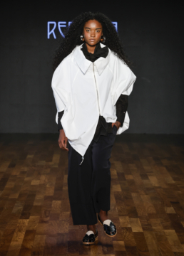 Modelo na passarela usando look preto e branco assimétrico da Reptília, com camisa de gola alta e saia fluida.