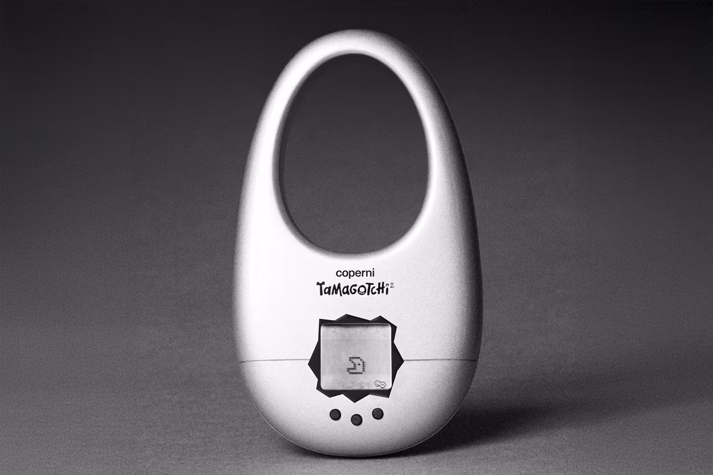 Bolsa prata da Coperni com Tamagotchi embutido, apoiada sobre superfície cinza com fundo neutro.