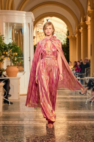 Modelo desfila no salão do Villa D’Este com macacão de tafetá rosa e capa esvoaçante, Chanel Cruise 2025/26.