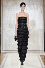 Modelo usando um vestido preto tomara que caia, coberto por camadas de franjas reluzentes. A silhueta alongada e o movimento do tecido criam um efeito impactante.