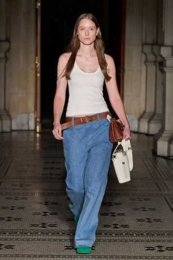 A modelo usa regata branca e calças jeans, com cinto marrom.