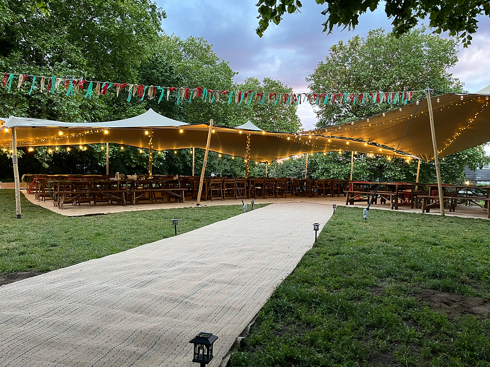 Stretch tent setup with matting walkway, festoon lighting & rustic furniture.