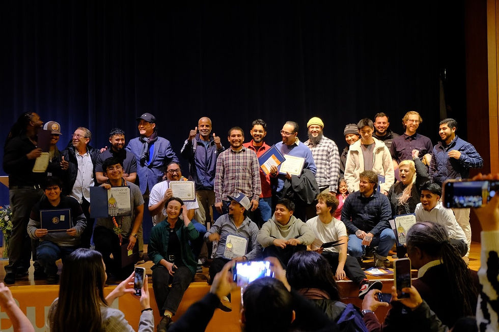 Group of CityBuild graduates on stage, some holding certificates, smiling for photos. Dark curtain backdrop. Bright, joyful atmosphere.