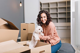 moving-new-modern-apartment-joyful-young-woman-finding-little-white-dog-carton-box-smiling