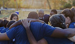 Group of people huddle together, arms around each other, in a park.