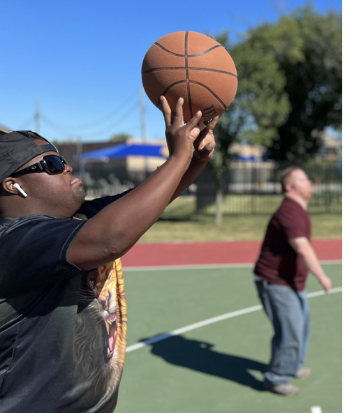 Man shooting basketball with blurred person in the background, Park Lawn.