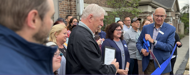 Man cuts blue ribbon as crowd watches, Park Lawn ribbon cutting event.
