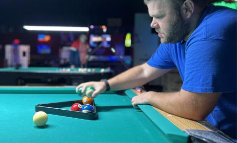 Man setting up pool balls, focused. Green table and dim bar setting.
