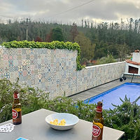 An outdoor table for al fresco dining with a couple of local beer, playing cards and popcorn in a bowl overlooking the saltwater pool and greenery in the garden at our Portugal rental home near Costa Nova.