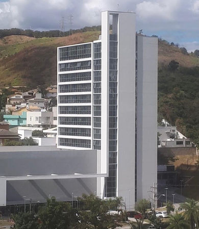 Vista externa do prédio de múltiplos andares onde fica o consultório da Janaina, cercado por montanhas e arquitetura imponente.