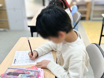 英語教室で小学生がプリントに英語を書いている様子